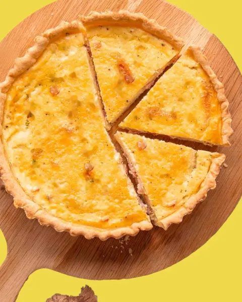 Quiche inteira fatiada sobre tábua de madeira, em fundo amarelo-limão